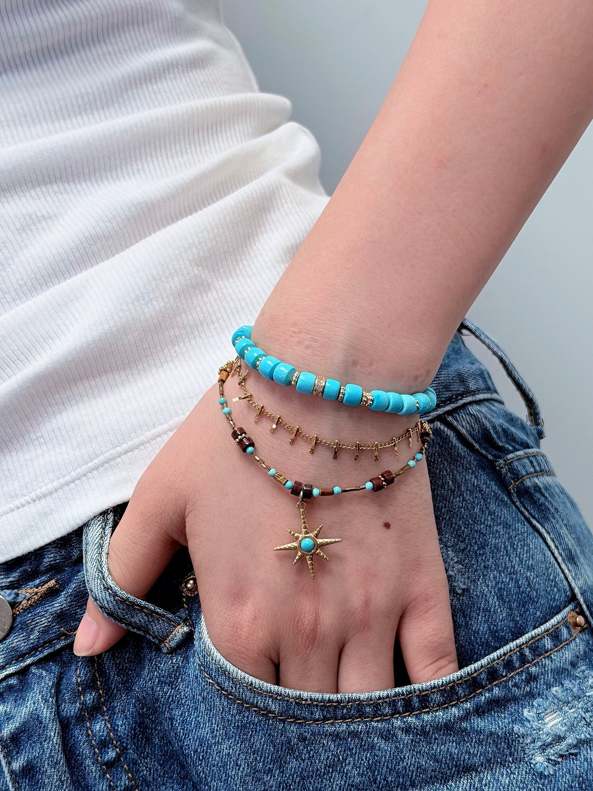 Turquoise beaded bracelet layered with gold jewelry